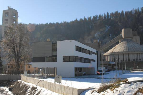 Aussenansicht. Hinter dem Neubau ist das Zementwerk zu erkennen. Um das Gebäude liegt Schnee. Die Stirnseite des Gebäudes ist im Treppenhaus mit durchgängigen Fenstern versehen und links oben sind im Kontrast zur weißen Putzfassade, graue Fassadenplatten angebracht. Aussenansicht. Hinter dem Neubau ist das Zementwerk zu erkennen. Um das Gebäude liegt Schnee. Die Stirnseite des Gebäudes ist im Treppenhaus mit durchgängigen Fenstern versehen und links oben sind im Kontrast zur weißen Putzfassade, graue Fassadenplatten angebracht.