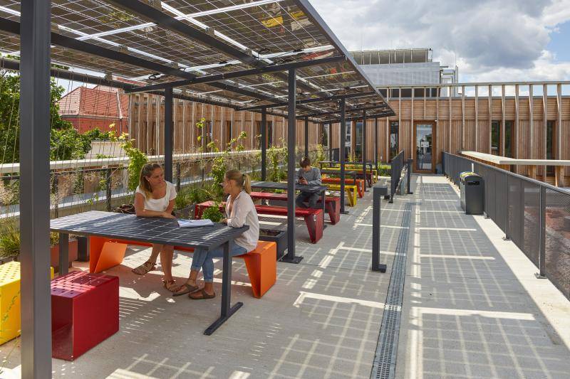Auf der Dachterrasse sind Dächer aus Solarpaneelen, unter denen sich Tische mit Bänken befinden. Auf der Dachterrasse sind Dächer aus Solarpaneelen, unter denen sich Tische mit Bänken befinden.
