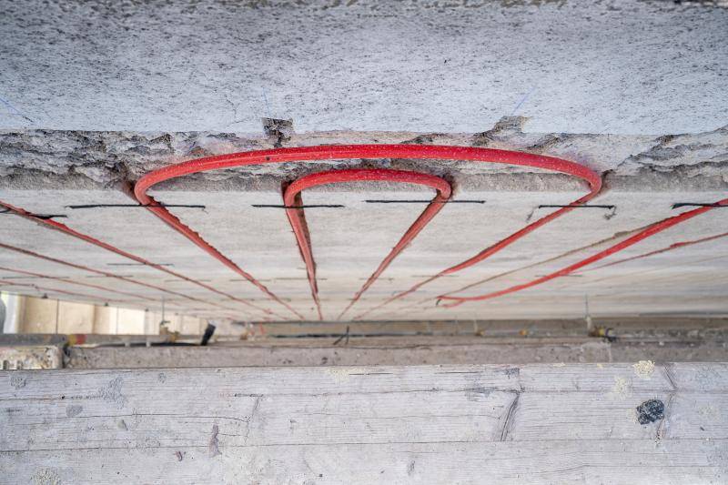 Bild von oben nach unten fotografiert zwischen Gerüst und Fassade. Zu sehen sind die eingefrästen roten Heiz-/Kühlleitungen, die ganz oben einen halb Kreis machen und wieder zurück nach unten verlaufen.