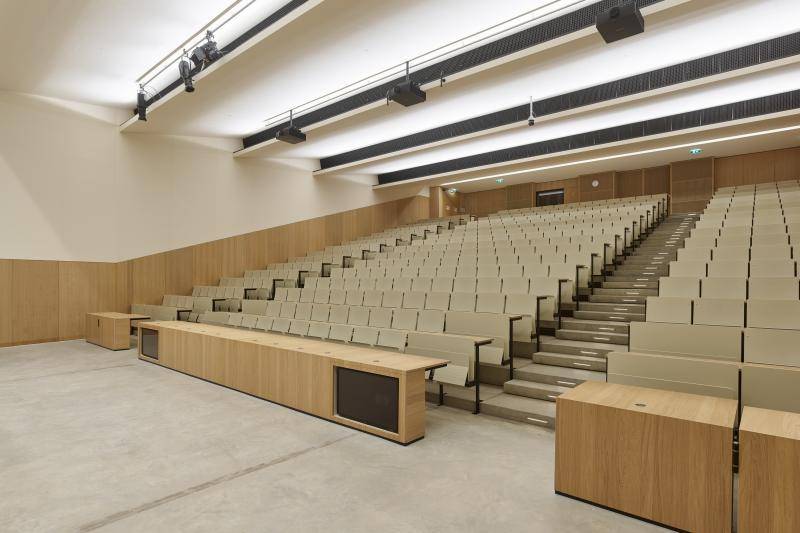 Ein Hörsaal mit Tribünenartiger Bestuhlung. Die Wändehalbhoch mit Holzverkleidung. Sichtbarer Estrich als Bodenbelag. Ein Hörsaal mit Tribünenartiger Bestuhlung. Die Wändehalbhoch mit Holzverkleidung. Sichtbarer Estrich als Bodenbelag.