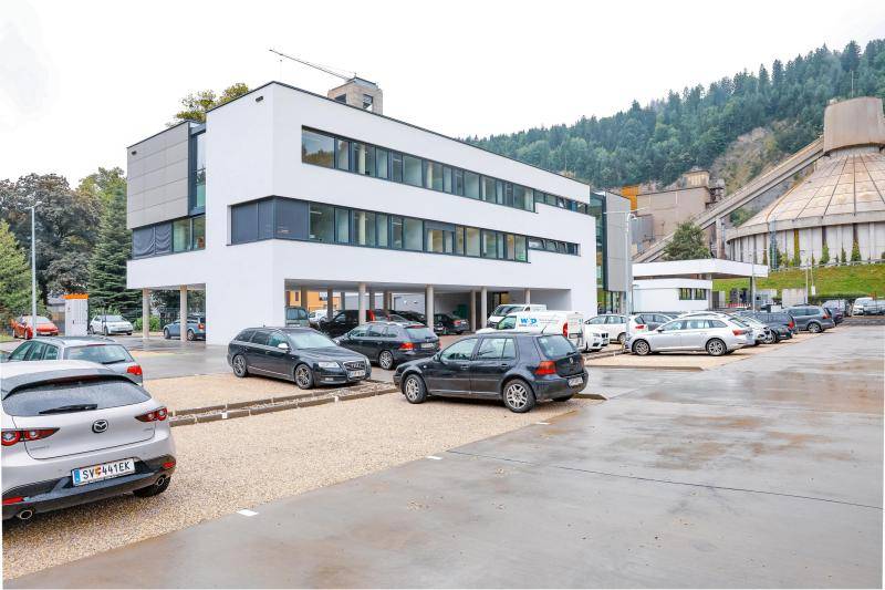 Ansicht vom Parkplatz auf das Gebäude. Im Hintergrund ist das Zementwerk zu sehen.