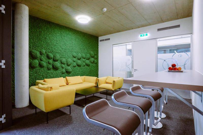 Aufenthaltsraum mit gelben Sitzmöbeln, sowie einer grünen, bemoosten Wand dahinter.