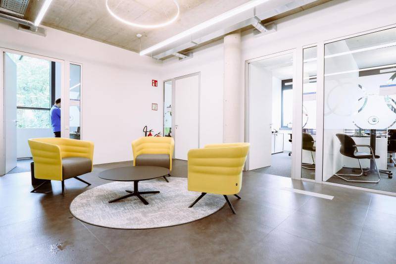 Flurbereich mit kleinem Tisch, an dem drei Sessel platziert sind. Im Hintergrund Büroräume.