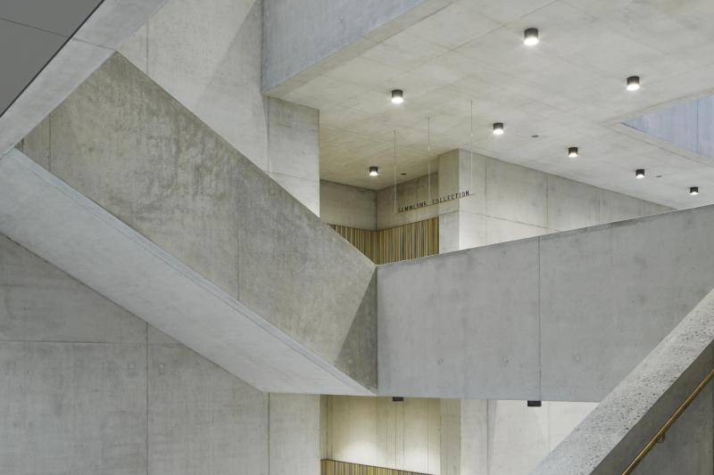 Zu sehen ist das Treppenhaus des Neubaus. Das gesammte Treppenhaus inklusive der Treppe selbst besteht aus Sichtbeton. Auch das massive Treppengeländer ist aus Beton. Der Belag der Treppe ist aus hellem Marmor gefertigt. Einzelne Akzente werden durch den goldenen Handlauf oder partielle Innenwandverkleidungen in Gold gesetzt. Die Beleuchtung sind kleine Runde LED_Lampen an den Decken. Zu sehen ist das Treppenhaus des Neubaus. Das gesammte Treppenhaus inklusive der Treppe selbst besteht aus Sichtbeton. Auch das massive Treppengeländer ist aus Beton. Der Belag der Treppe ist aus hellem Marmor gefertigt. Einzelne Akzente werden durch den goldenen Handlauf oder partielle Innenwandverkleidungen in Gold gesetzt. Die Beleuchtung sind kleine Runde LED_Lampen an den Decken.