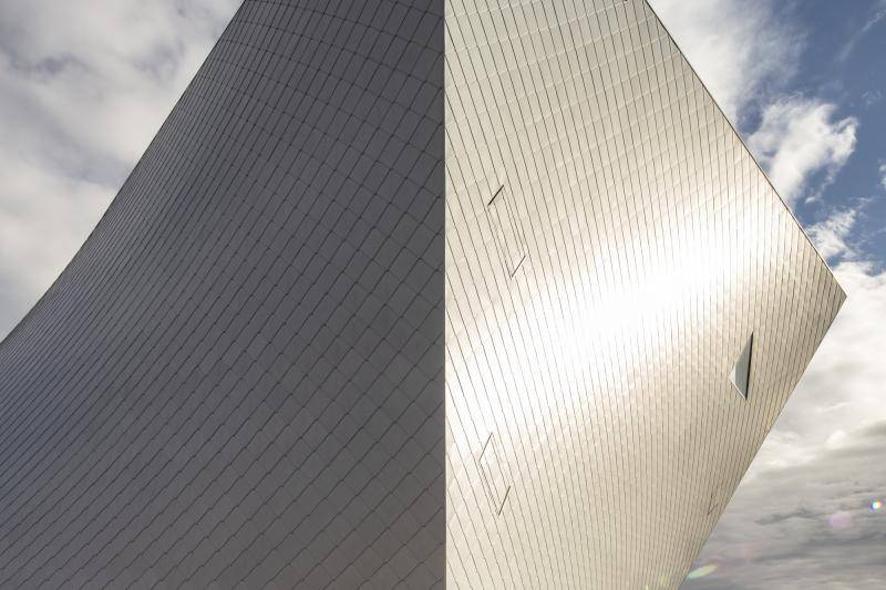 Das Gebäudeeck an dem zwei der Fassaden spitz zusammen laufen ist zu sehen. Eine der Seiten glänzt im Sonnenlicht, die Andere liegt im Schatten.