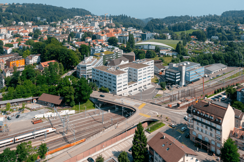Das Gebäude aus der Luft aufgenommen. Es ist hinter den Bahngleisen sowie hinter einer Brücke über diese, gelegen. Das Gebäude aus der Luft aufgenommen. Es ist hinter den Bahngleisen sowie hinter einer Brücke über diese, gelegen.