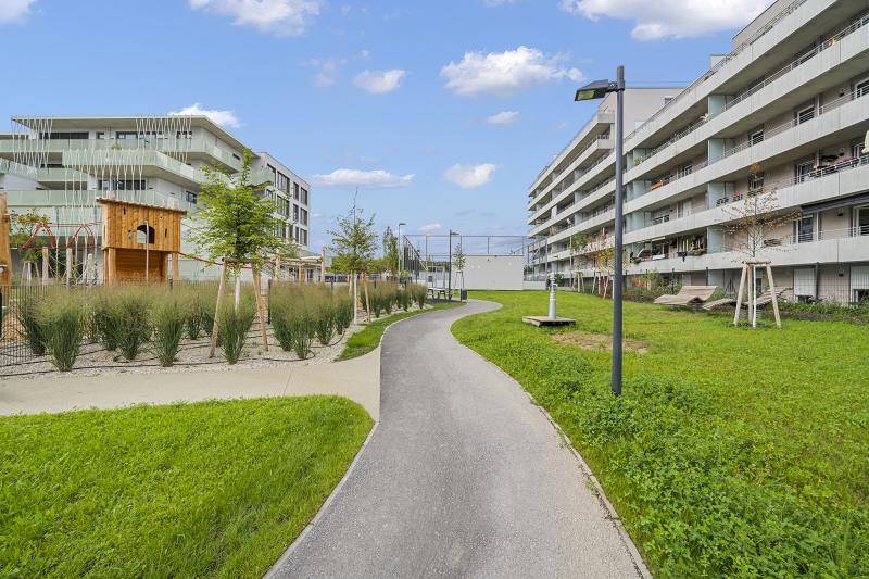 Ein Fußweg, der außerhalb des Grundstücks verläuft. Rechts sind die Balkone des Gebäudes zu sehen. Um den Weg ist Alles begrünt und ein Spiel- und Sportplatz ist angelegt. Ein Fußweg, der außerhalb des Grundstücks verläuft. Rechts sind die Balkone des Gebäudes zu sehen. Um den Weg ist Alles begrünt und ein Spiel- und Sportplatz ist angelegt.