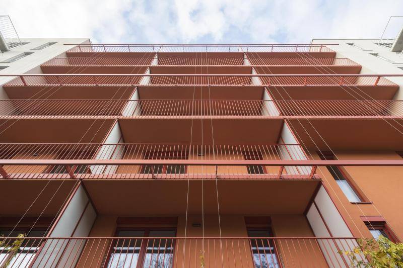 Ein Orangener Gebäudeteil wird von unten nach oben fotografiert. Die Balkongeländer wirken durchlaufend über Alle Geschosse. Durch die dünnen Geländerteile verschwindet das Geländer optisch in der Fassade und fällt kaum auf. Ein Orangener Gebäudeteil wird von unten nach oben fotografiert. Die Balkongeländer wirken durchlaufend über Alle Geschosse. Durch die dünnen Geländerteile verschwindet das Geländer optisch in der Fassade und fällt kaum auf.