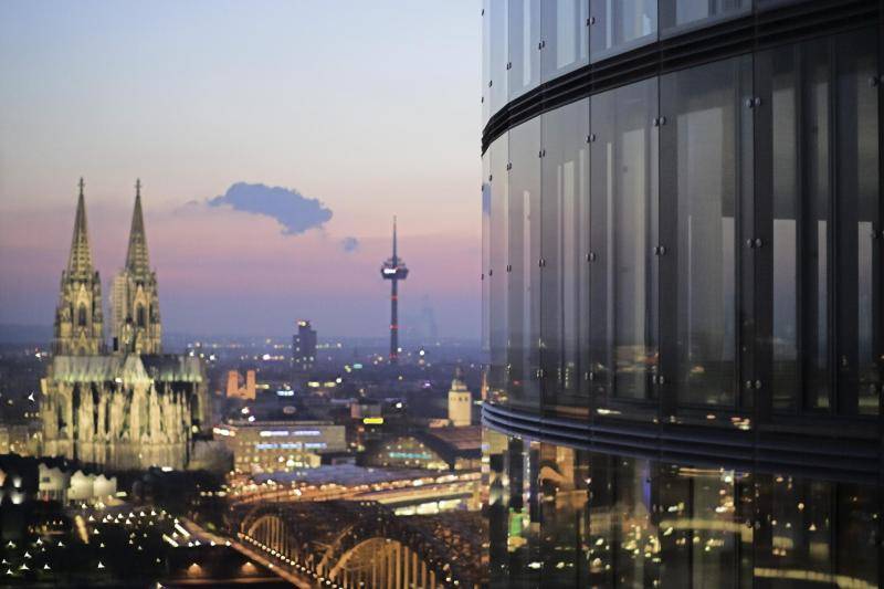 Die rechte Hälfe des Bildes zeigt die Glasfassade des Turms. Links sieht man Den Köllnerdom in der Dämmerung, der beleuchtet ist, sowie den Rhein und den Fernsehturm. Die rechte Hälfe des Bildes zeigt die Glasfassade des Turms. Links sieht man Den Köllnerdom in der Dämmerung, der beleuchtet ist, sowie den Rhein und den Fernsehturm.