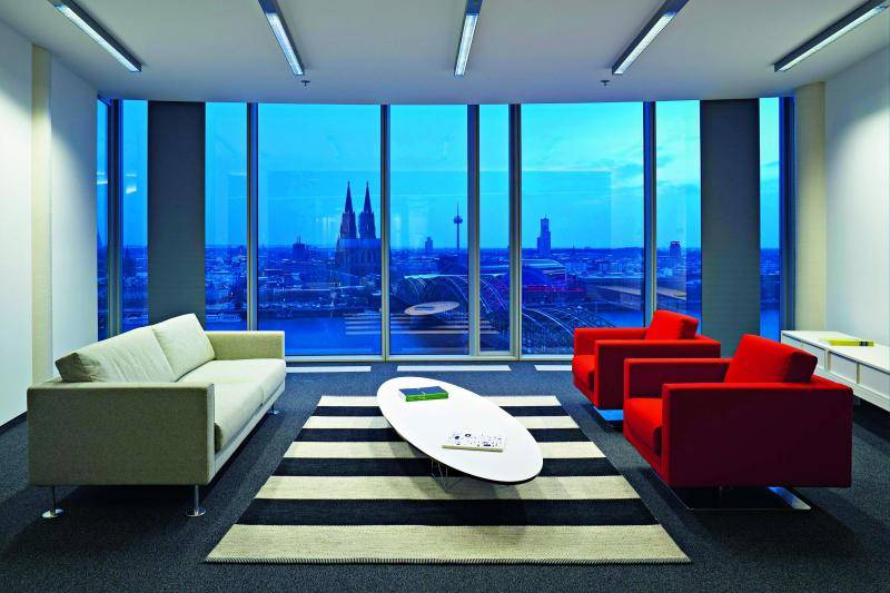 Innenaufnahme eines Aufenthaltsraumes. Zwei Sofas sind zu sehen in rot und weiß. Kleiner Tisch dazwischen. Durch die Fenster sieht man den Dom und die Stadt. Innenaufnahme eines Aufenthaltsraumes. Zwei Sofas sind zu sehen in rot und weiß. Kleiner Tisch dazwischen. Durch die Fenster sieht man den Dom und die Stadt.