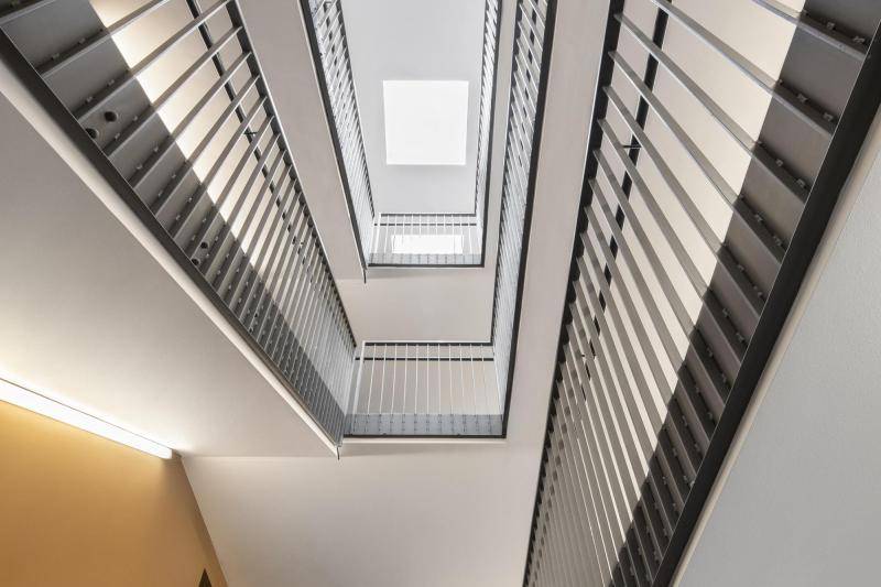 Das Treppenhaus mit seinem rechteckigen Treppenauge wird von unten nsenkrecht nach oben fotografiert. weiße Treppenunterseiten und graue Geländer sind zu sehen Das Treppenhaus mit seinem rechteckigen Treppenauge wird von unten nsenkrecht nach oben fotografiert. weiße Treppenunterseiten und graue Geländer sind zu sehen