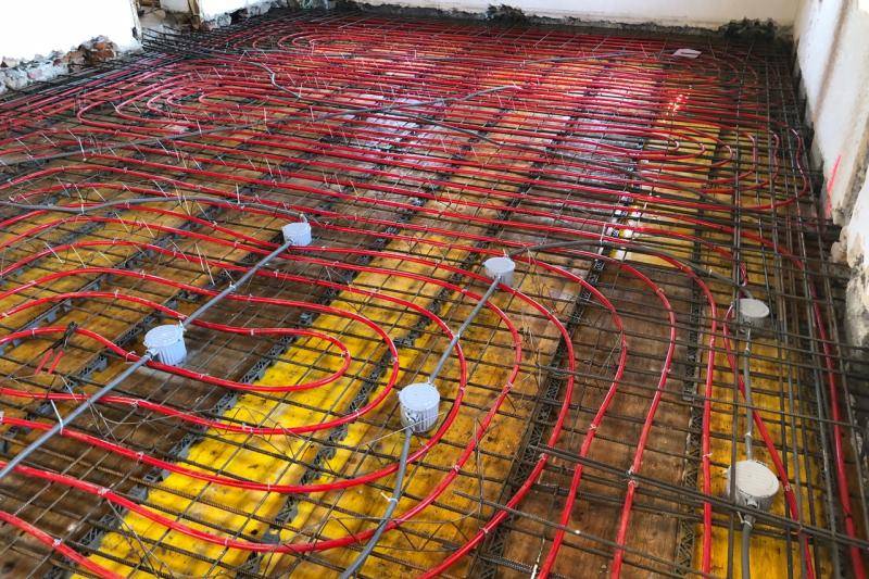 Auf gelben Schalungsplatten sind rote Schläuche verlegt. Um die Deckenschalung sind die alten weißen Wände des Raums zu sehen. Auf gelben Schalungsplatten sind rote Schläuche verlegt. Um die Deckenschalung sind die alten weißen Wände des Raums zu sehen.
