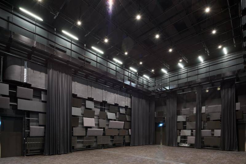 Dieser Raum ist schwarz ausgekleidet. An den Wänden hängen Rechteckige Akkustik Elemente in unterschiedlichen Grüßen und Ausführungen. Dazwischen hängen schwarze Vorhänge. Oben entlang läuft ein Laufsteg aus schwarzem Metall und die Decke ist mit einem Gerüst für Lichter ausgestattet. Dieser Raum ist schwarz ausgekleidet. An den Wänden hängen Rechteckige Akkustik Elemente in unterschiedlichen Grüßen und Ausführungen. Dazwischen hängen schwarze Vorhänge. Oben entlang läuft ein Laufsteg aus schwarzem Metall und die Decke ist mit einem Gerüst für Lichter ausgestattet.