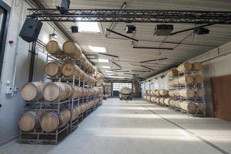 In einem Lagerraum sind links und rechts an den Wänden große Regale in denen Holzfässer gelagert sind. Der Raum ist sehr hell, durch Oberlichter an der Decke. In einem Lagerraum sind links und rechts an den Wänden große Regale in denen Holzfässer gelagert sind. Der Raum ist sehr hell, durch Oberlichter an der Decke.