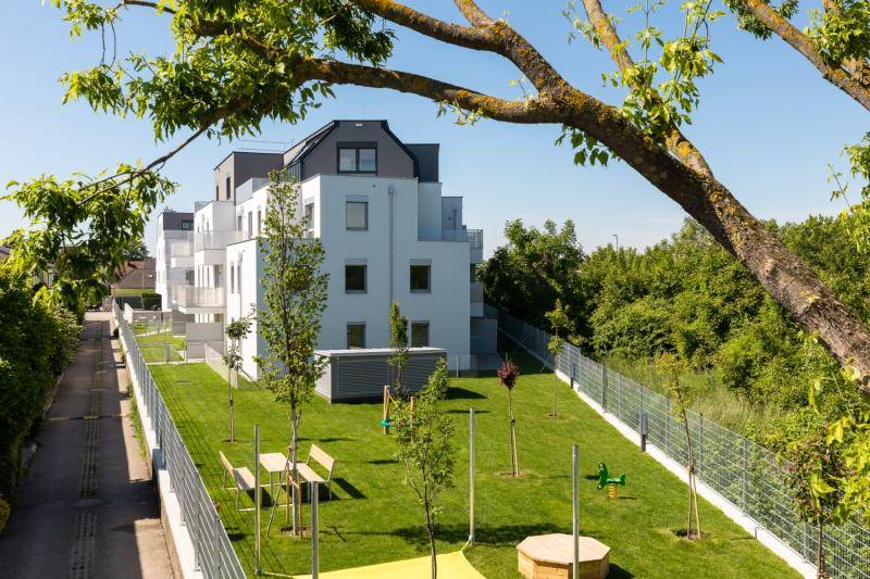 Blick aus der Distanz auf die Stirnseite des Hauses. Im Gartenteil sind Tisch und Bänke, sowie einige Spielgeräte. Junge Bäume wurden angepflanzt.