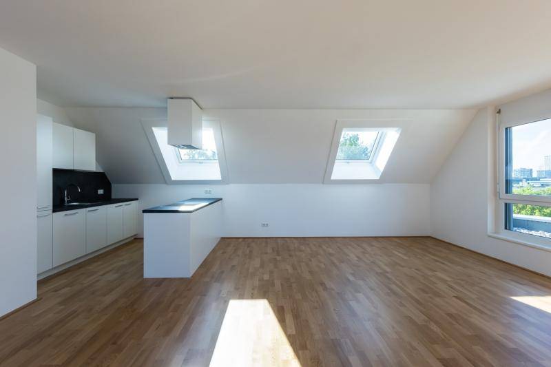 Eine Dachgeschosswohnung mit offener Küche. Natürliche Belichtung durch Dachflächenfenster. Parkettboden. Küche sowie Wandoberflächen in weiß.