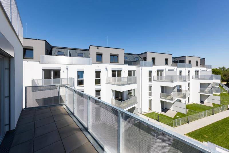 Blick von einem oberen Balkon auf den daneben liegenden Bau. Um die Gebäude sind grünflächen, sowie ein Weg.