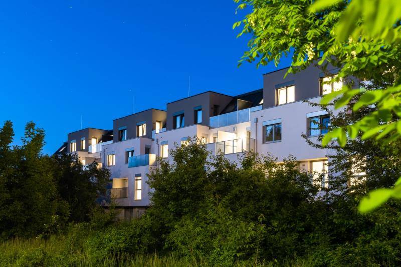 Aufnahme in der Dämmerung. Die Balkone sind mit Außenlampen beleuchtet.