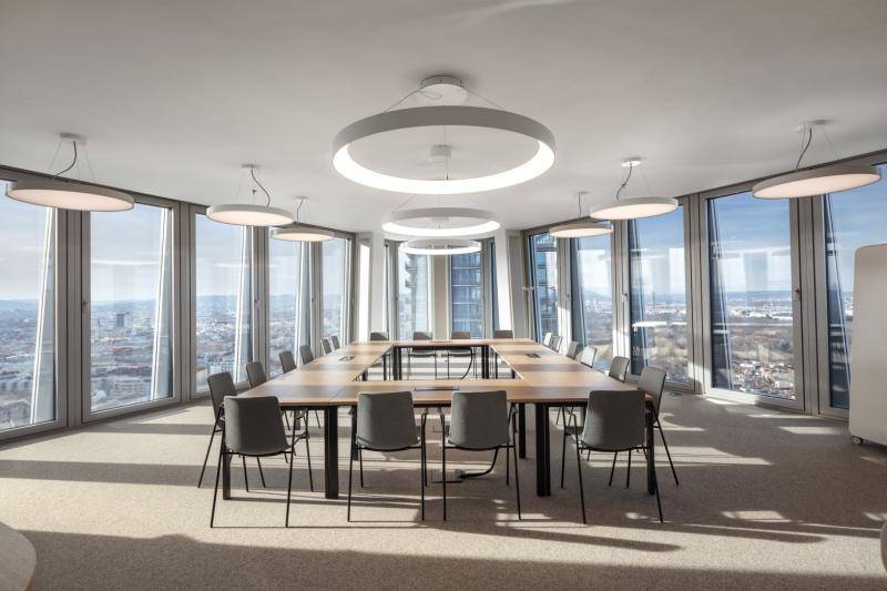 Besprechungsraum im spitz zulaufenden Gebäudeteil. Große, kreisförmige Lampen an der Decke. Ausblick auf die umliegenden Gebäude in allen Richtungen. Besprechungsraum im spitz zulaufenden Gebäudeteil. Große, kreisförmige Lampen an der Decke. Ausblick auf die umliegenden Gebäude in allen Richtungen.