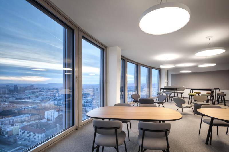 Aufenthaltsraum mit Tischen und Stühlen vor raumhohen Fenstern mit Blick über die Stadt. Aufenthaltsraum mit Tischen und Stühlen vor raumhohen Fenstern mit Blick über die Stadt.