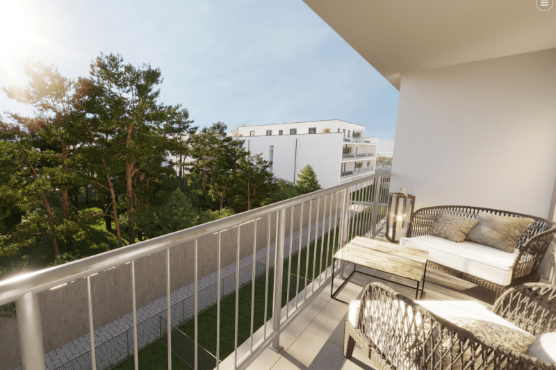Blickvon einem Balkon ins Grüne. Es sind viele Bäume zu sehen, sowie ein weiteres Wohngebäude dahinter. Auf dem Balkon befinden sich Gartenmöbel.