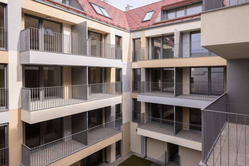 Blick in den Innenhof. Grasflächen und ein gepflasterter Weg sinddort zu sehen. Große Balkone sind am Gebäude. Das Dach ist in roter Farbe gedeckt. Blick in den Innenhof. Grasflächen und ein gepflasterter Weg sinddort zu sehen. Große Balkone sind am Gebäude. Das Dach ist in roter Farbe gedeckt.