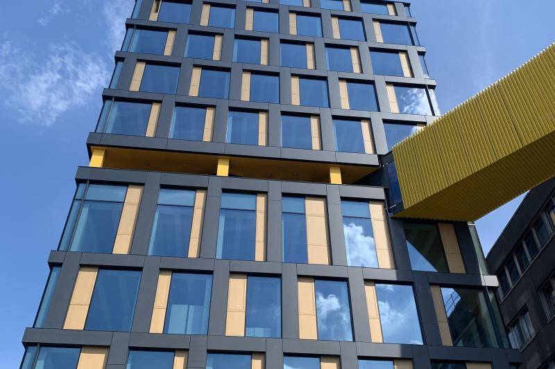 Die Fassade des Gebäude besteht aus großen, rechteckigen Fenstern neben denen Gelbe Rechtecke, farbliche Akzente setzen in der grauen Fassade. Das Gebäude hat 9 Stockwerke. Von rechts schließt sich ein Übergang an das Gebäude an. Dieser ist mit gelben Elementen verkleidet und nicht zu durchblicken. Die Fassade des Gebäude besteht aus großen, rechteckigen Fenstern neben denen Gelbe Rechtecke, farbliche Akzente setzen in der grauen Fassade. Das Gebäude hat 9 Stockwerke. Von rechts schließt sich ein Übergang an das Gebäude an. Dieser ist mit gelben Elementen verkleidet und nicht zu durchblicken.