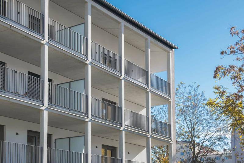 Das Gebäude in Sichtbeton ist auf seiner gesammten Länge mit Balkonen versehen. Die Mischung aus Betonoberflächen und weißem Putz lassen das Gebäude sehr hell wirken. Das Gebäude in Sichtbeton ist auf seiner gesammten Länge mit Balkonen versehen. Die Mischung aus Betonoberflächen und weißem Putz lassen das Gebäude sehr hell wirken.