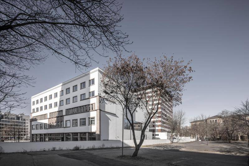 Im Bildzentrum ist ein Blattloser Baum zu sehen. Dahinter sieht man das Deutschlandhaus den Langenseite nach. Zu sehen ist die weiße Fassade mit Fesnterlaibungen aus hellemNaturstein und Rahmen wieder in weiß. Das Gebäudeeck ist abgerundet in Form einer herrausstehenden Säule aus Naturstein. Umgeben ist das Gebäude von einer ca. 1m hohen Mauer in weiß. Im Bildzentrum ist ein Blattloser Baum zu sehen. Dahinter sieht man das Deutschlandhaus den Langenseite nach. Zu sehen ist die weiße Fassade mit Fesnterlaibungen aus hellemNaturstein und Rahmen wieder in weiß. Das Gebäudeeck ist abgerundet in Form einer herrausstehenden Säule aus Naturstein. Umgeben ist das Gebäude von einer ca. 1m hohen Mauer in weiß.